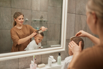 Portrait of caring Caucasian mother combing hair or mixedrace baby boy by mirror in bathroom, copy space - Powered by Adobe