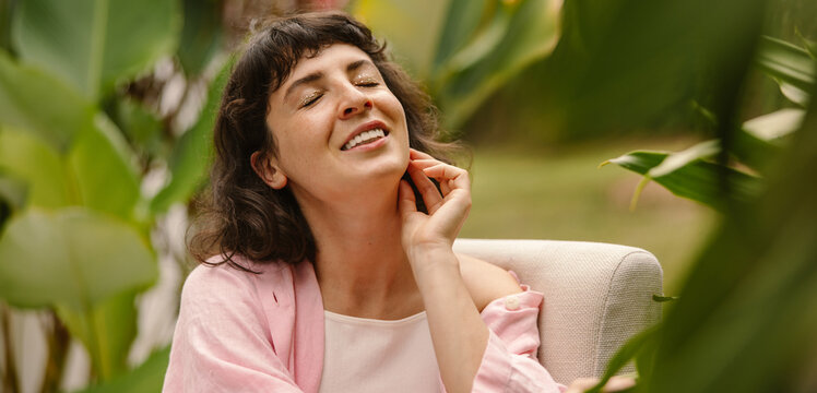 Calm young caucasian woman relaxes with her eyes closed enjoying easy chair outdoors. Brunette with bob haircut wearing pink shirt. Lifestyle, different emotions, leisure concept.