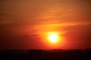 Sunset on a red sky with evening clouds in the city. The setting evening sun over the city with high-rise buildings