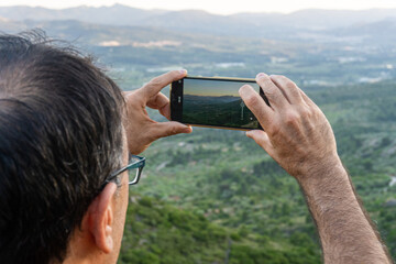 Rear view of a man taking photos with the phone of a natural landscape.