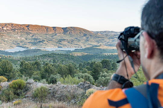 Rear view of a out of focus man taking photos of a mountainous landscape at sunset.