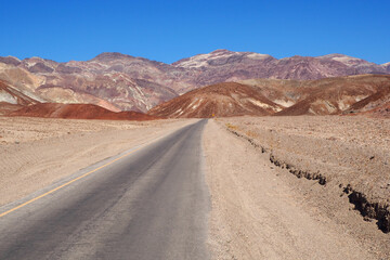 Fototapeta na wymiar Asphalt road leading through steaming hot landscape of Death Valley National Park, California, USA. Super hot sunny day in the desert of the southwest. Vast land of dirt and dust.