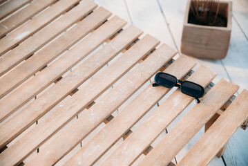 Summer holiday concept, sunglasses in black color lie on a wooden deck chair.
