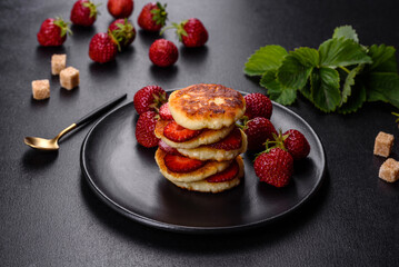 Cottage cheese pancakes with sliced strawberries and strawberry jam on a plate on a concrete background