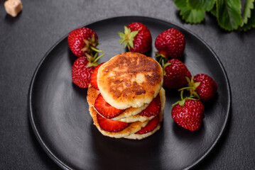 Cottage cheese pancakes with sliced strawberries and strawberry jam on a plate on a concrete background