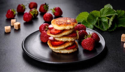 Cottage cheese pancakes with sliced strawberries and strawberry jam on a plate on a concrete background