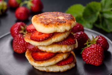 Cottage cheese pancakes with sliced strawberries and strawberry jam on a plate on a concrete background