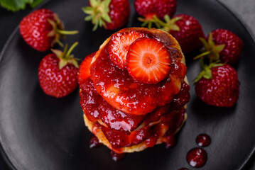 Cottage cheese pancakes with sliced strawberries and strawberry jam on a plate on a concrete background