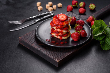 Cottage cheese pancakes with sliced strawberries and strawberry jam on a plate on a concrete background