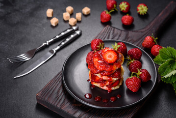 Cottage cheese pancakes with sliced strawberries and strawberry jam on a plate on a concrete background