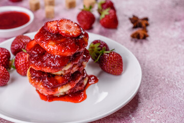 Cottage cheese pancakes with sliced strawberries and strawberry jam on a plate on a concrete background