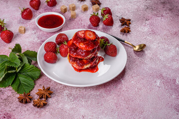 Cottage cheese pancakes with sliced strawberries and strawberry jam on a plate on a concrete background