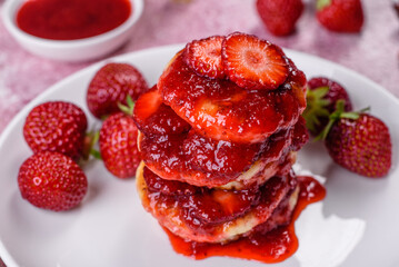 Cottage cheese pancakes with sliced strawberries and strawberry jam on a plate on a concrete...