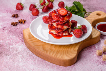 Cottage cheese pancakes with sliced strawberries and strawberry jam on a plate on a concrete background
