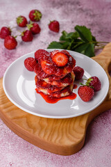Cottage cheese pancakes with sliced strawberries and strawberry jam on a plate on a concrete background