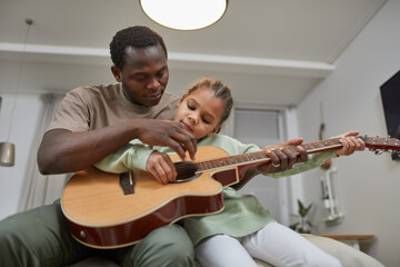 Portrait of loving black father playing guitar with cute little girl at home, copy space