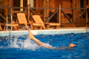 Woman swims in a pool with clear water on the background of a summer sunset on vacation