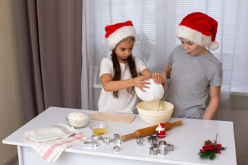 Children in red caps, stand at a white kitchen table, prepare dough in a bowl with interest in the kitchen