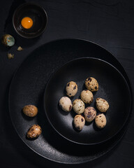 Quail eggs in a black plates on the black background. Top view. Free copy space.