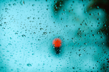 Luz roja de semáforo desenfocada con gotas de lluvia en una ventana en primer plano