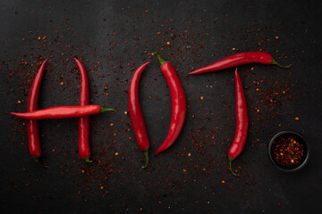 Word "HOT" is lined with red chilli pepper. Red peppers creating a word hot on black background.Top view. Free copy space.