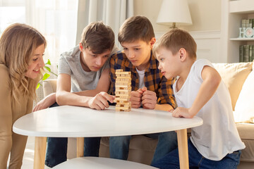 A smiling woman and three boys are enthusiastically playing a board game made of wooden rectangular...