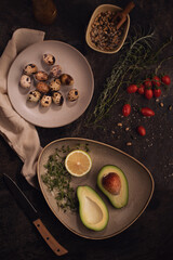 Ripe avacado decoreted on the plate and raw Quail eggs on the dark table.Healthy breakfast, vegetable food.