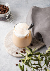 Cappuccino or latte with milk foam in a glass with coffee beans on light  marble background with branches. Top view