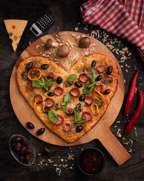 Wooden board with tasty heart-shaped pizza with ingredients on black background. Valentine's Day celebration.