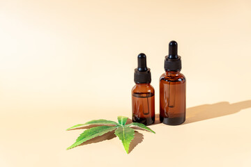 Glass dropper bottles with cbd oil on beige background with marijuana leaf. Hemp based cosmetics. Natural herbal hemp essential oil in a glass pipette bottle.