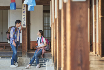 Obraz na płótnie Canvas 한국의 옛날 전통 가옥 건물을 배경으로 여행 또는 가이드 하고 있는 젊은 남녀 커플 또는 친구 아시아 모델