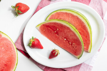 Summer berries, watermelon slices and strawberries on a platter on a white table.