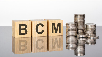 bcm - text on wooden cubes on a cold grey light background with stacks coins