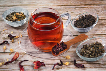 Cup of tea on wooden table with dry herb leaves of different tea.