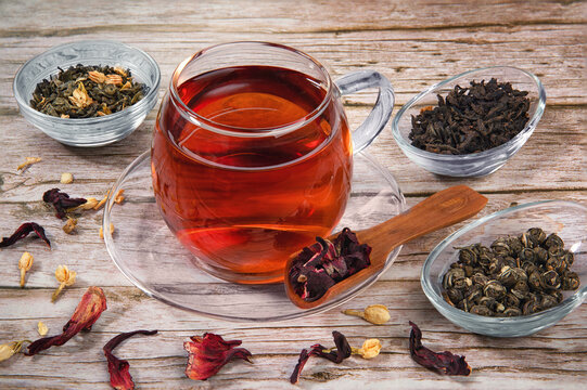 Cup of tea on wooden table with dry herb leaves of different tea.