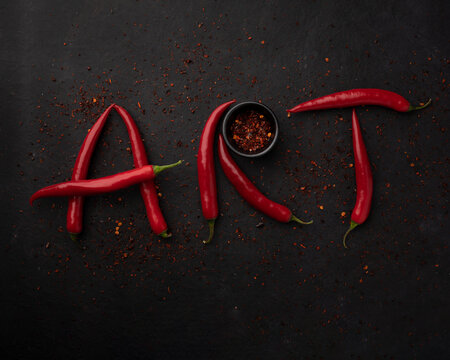Word "ART" is lined with red chilli pepper. Red peppers creating a word art on black background.Top view. Free copy space.