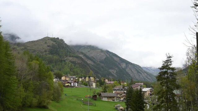 Beaulard, Piedmont, Italy. May 2022. Amazing tilt footage of the mountain township. Low spring clouds cover the top of the mountains that surround the valley. Mountain travel image.