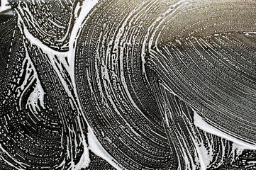 Background, texture of the black surface of a metal car door in white soapy foam after washing....