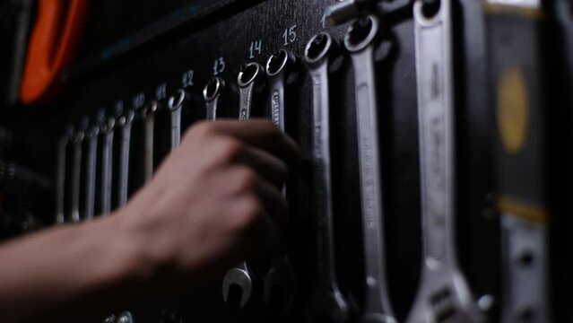 Close-up hands of unrecognizable repairman selecting wrench from instruments set of hanging on wall in repair shop. Auto or bicycle mechanic with working instrument tools for repair and diagnostics.