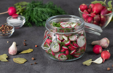 Sliced radish with dill in a glass jar on a dark table with spices and fresh ingredients