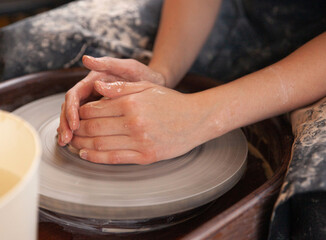 A woman works on a potter's wheel. Hands form a cup of wet clay on a potter's wheel. Artistic concept.