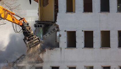 Close up of a bucket of an excavator demolishing an old building. Dangerous demolition works in the...