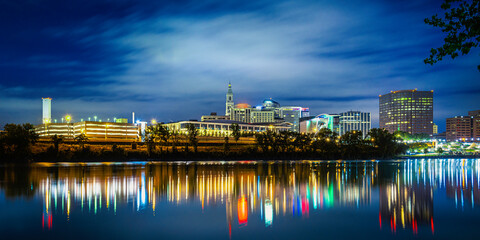 Fototapeta premium Nightscape and cityscape of downtown Hartford in Connecticut with glowing bokeh light reflections on the river water on a cloudy night.