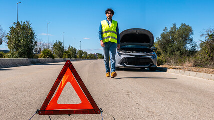 Young man preparing a red triangle to warn other road users of car breakdown