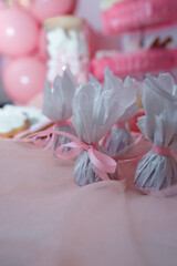 Baby girl first birthday candy bar. Chocolate candies wrapped in white paper with pink ribbons. Soft focused closeup shot