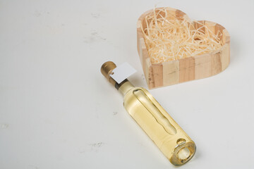 250 ml bottle of white wine with blank label on light background, copy space. Heart shaped box of wooden shavings.