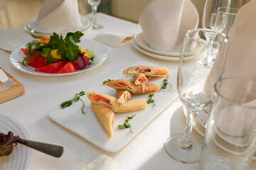 Festive table with appetizers. Pancakes with red fish salmon and microgreen. Fish appetizers before the main meal. Vegetable plate. Empty glasses for guests