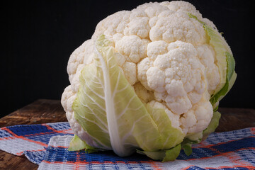 Cauliflower head on kitchen towel, wooden background. Organic farm vegetables, seasonal harvest,...