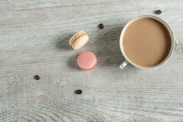 Fototapeta na wymiar A mug of coffee with milk on a gray wooden table with scattered macaroons. Top view, selective focus with copy space