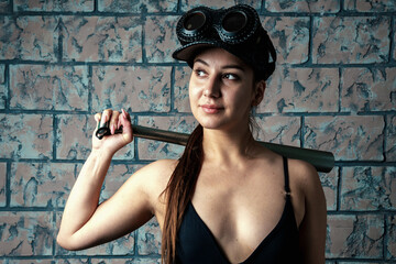 A young lady in a black cap and steampunk glasses holds a bat on her shoulder...